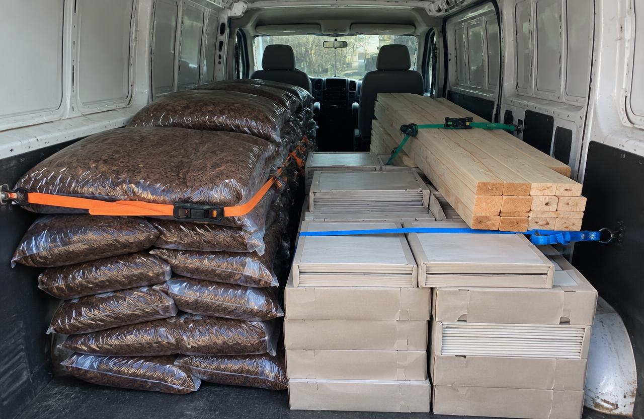 Inside a cargo van loaded with strapped-down lumber boards, boxed tiles, and stacked bags of mulch